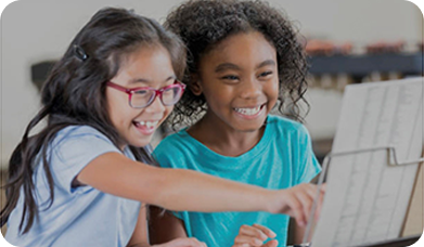 Two girls are smiling while looking at a laptop.